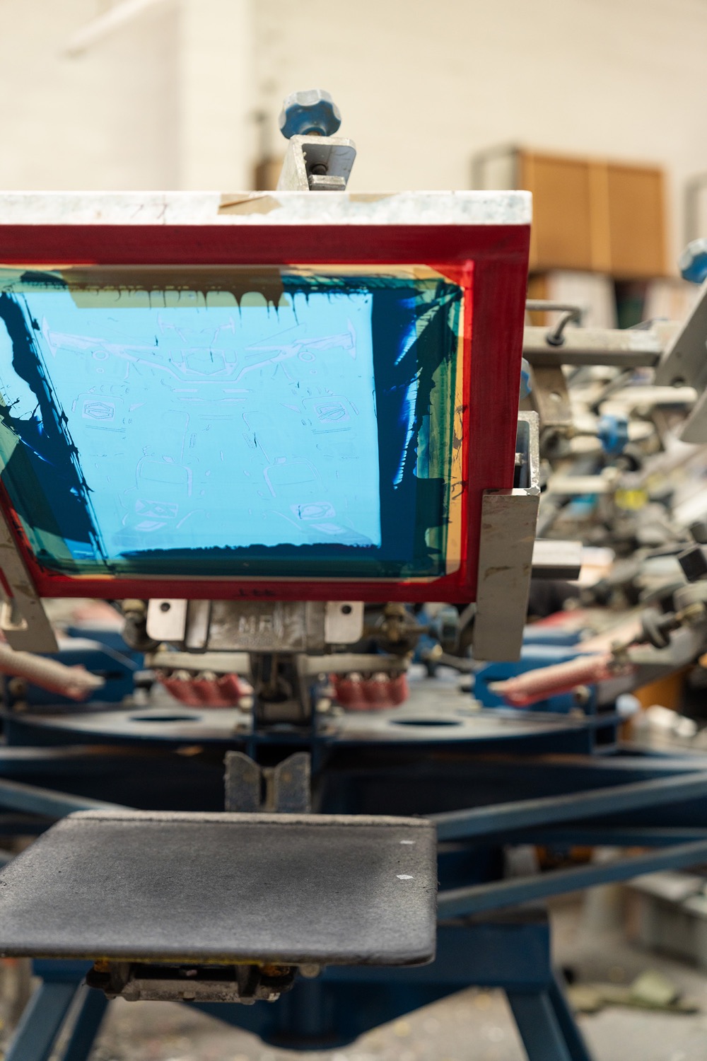 A blue screen printing press with an inked screen