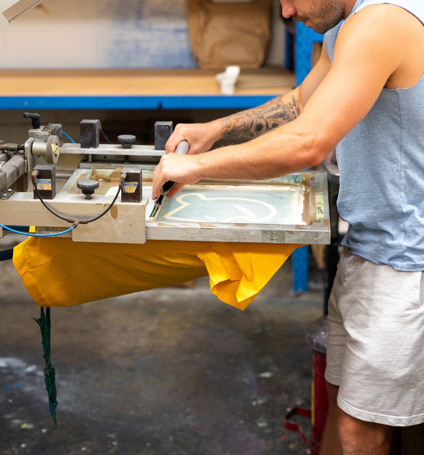 A printmaker pulling ink across a screen onto a yellow T-shirt